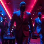 Figures in dark suits and masks walk through a neon-lit nightclub